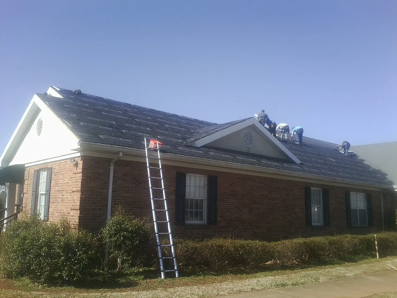 Crew tearing shingles off a brick ranch roof with a ladder set — Metal Roof Repair work by our crew in Woodsboro