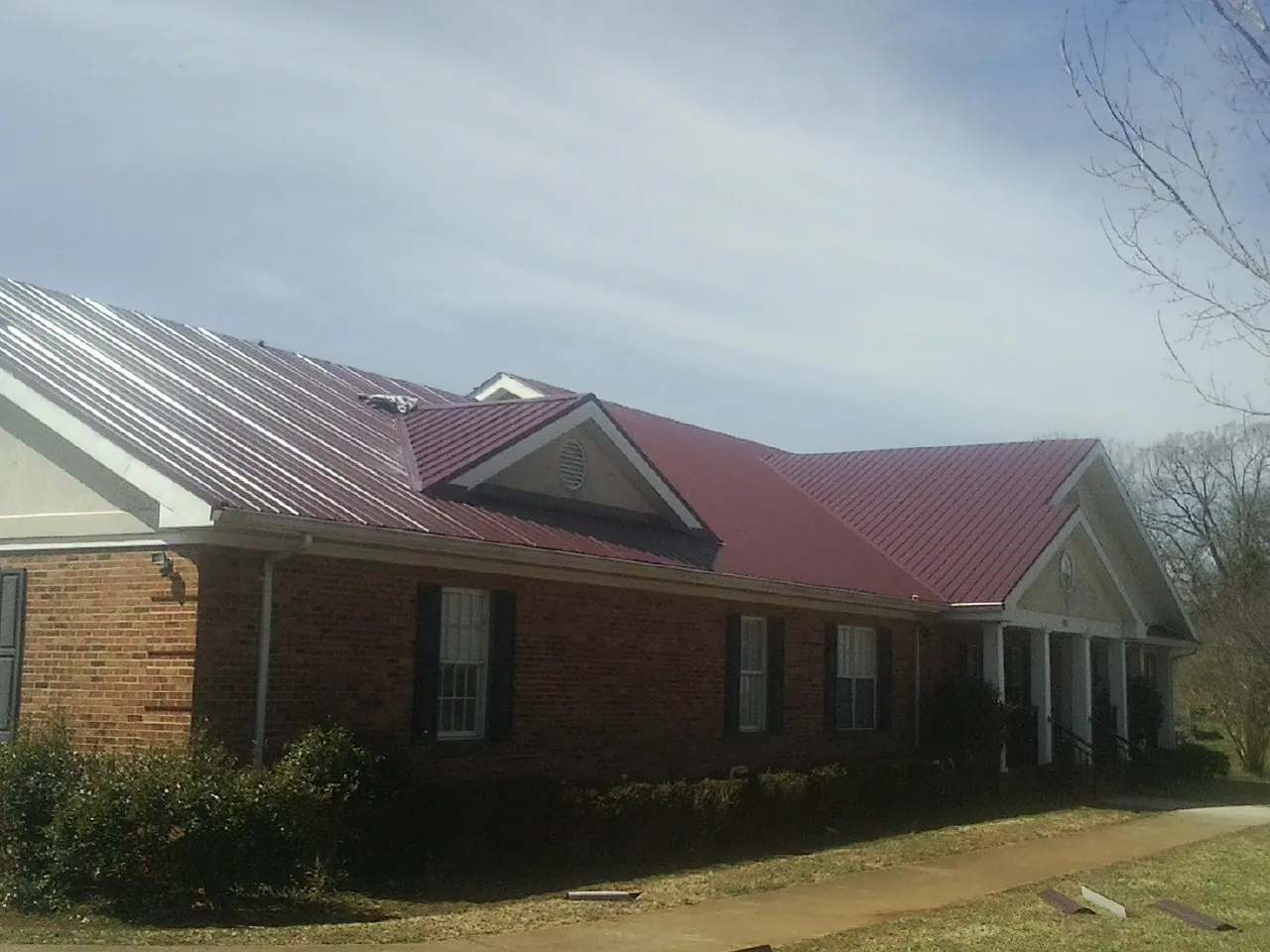 Red metal roof with gabled entries on a long brick building, from a Hail Damage Roof Repair job in Woodsboro