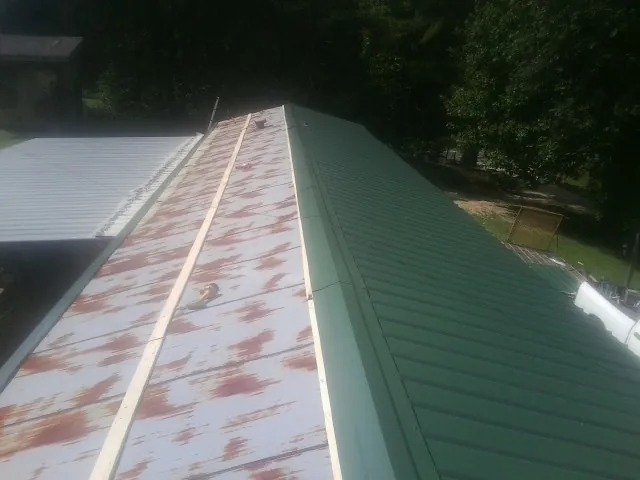 Old rusted panels beside newly installed green metal roofing — Wind Damage Roof Repair by Roofing Brothers in Woodsboro