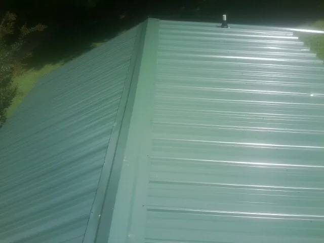 New green metal panels meeting at the ridge of a roof — Flat Roof Repair work by our crew in Woodsboro