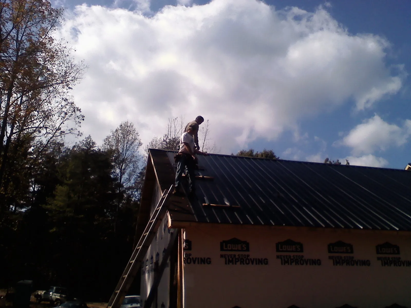 Roofer fastening dark metal panels high against a cloudy sky, from a Roof Inspection job in Woodsboro