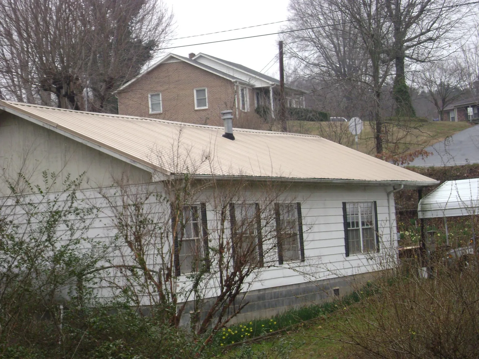 Tan metal roof on a white sided house set into a hillside — Commercial Roofing by Roofing Brothers in Woodsboro